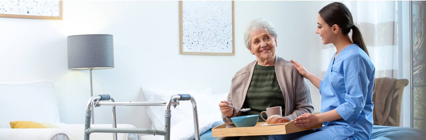elderly woman in a nursing home, sitting on a chair along side her nurse, both smiling and looks very happy. 