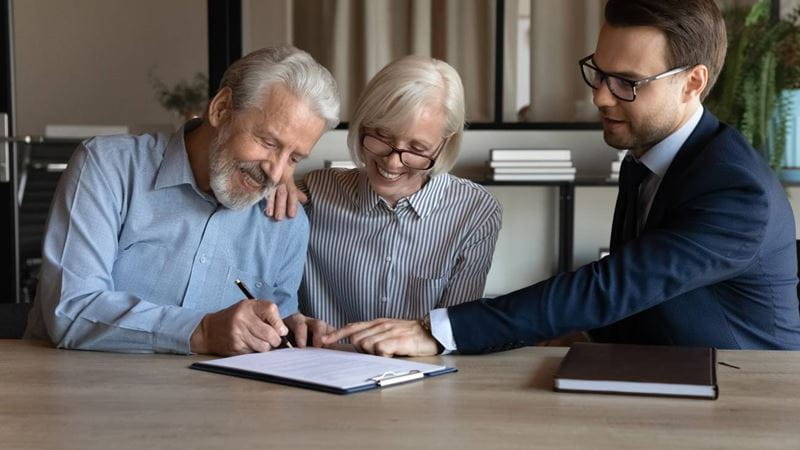 Mature couple sitting at a table with a lawyer signing a contract