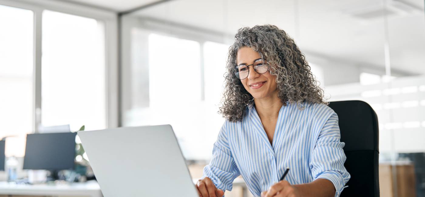 Smiling middle aged professional executive looking at computer, elearning, and writing notes