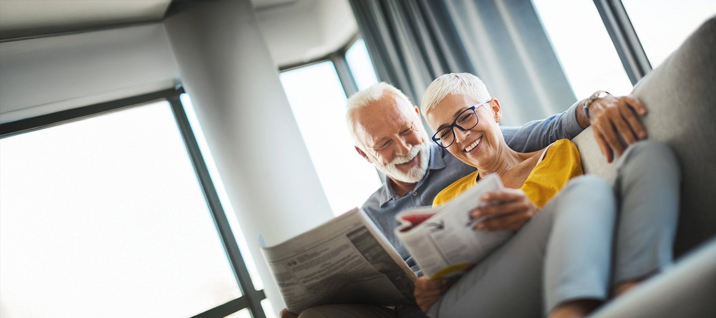 Mature happy couple sitting on a couch and reading magazines.