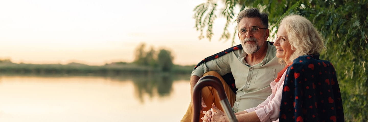 Mature couple relaxing on a pier, sharing a blanket and enjoying the sunset over the lake.
