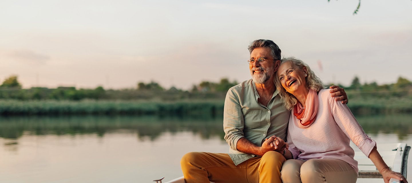 Mature couple holding hands and laughing while enjoying a romantic boat trip on the lake at sunset