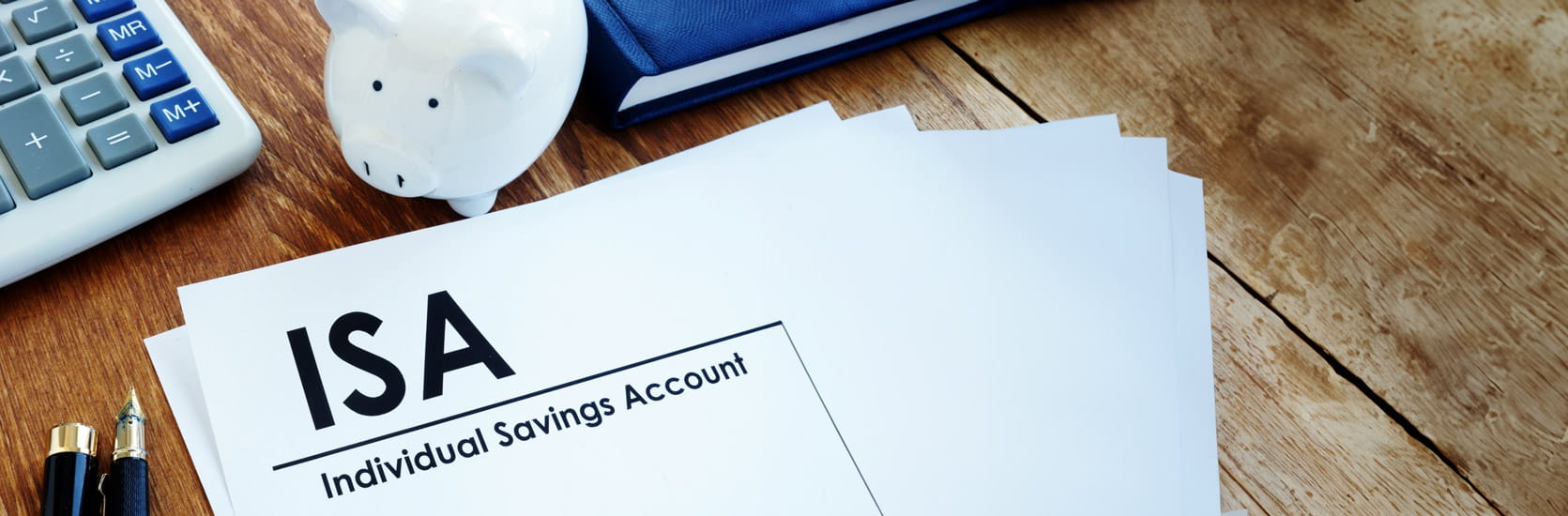 A desk with a computer, a piggy bank and some paperwork with the word Individual Savings Account printed at the top