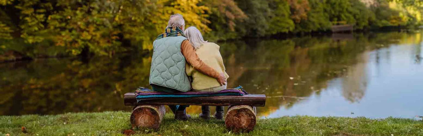 Two people sat on a bench looking out over a lake in autumn