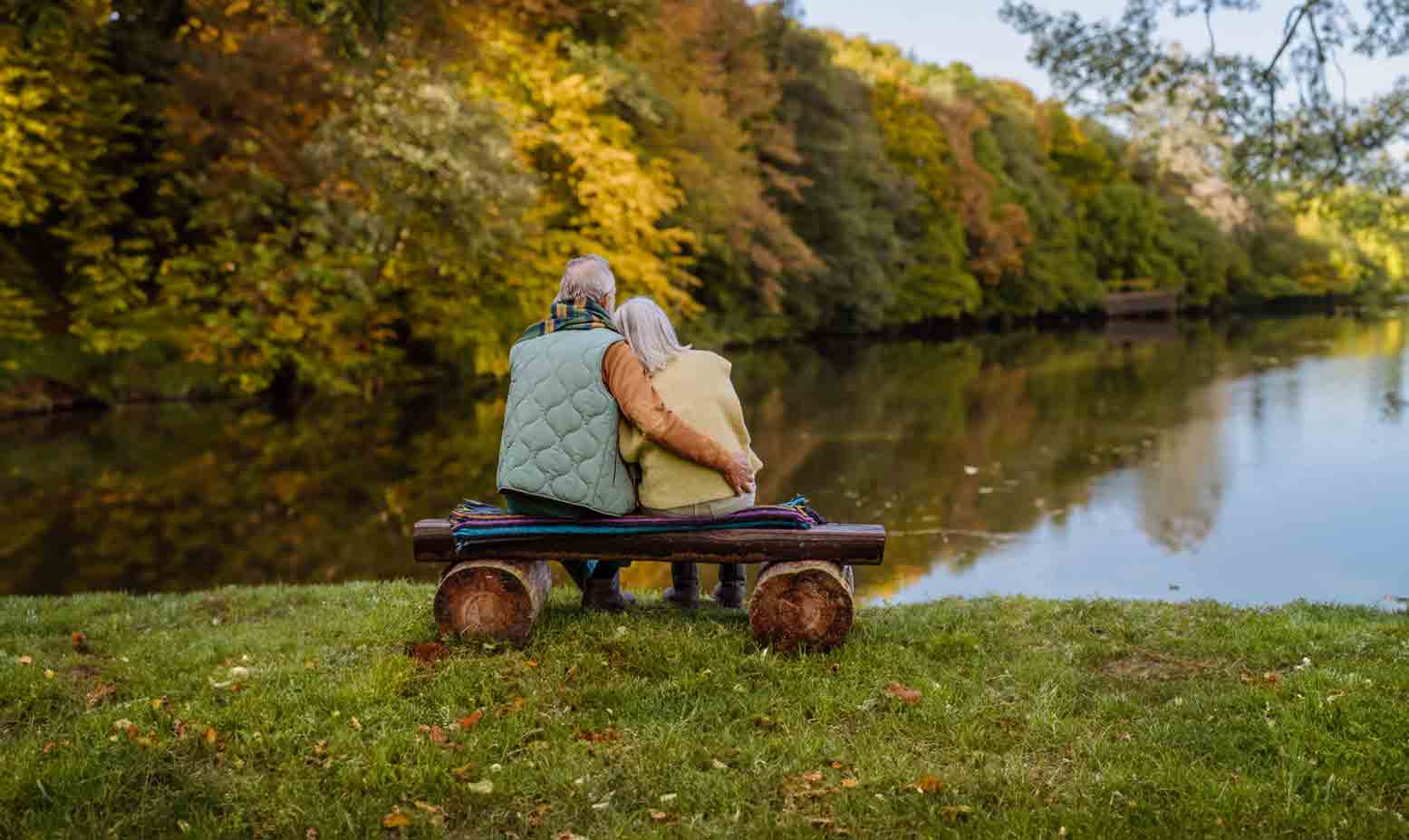 Two people sat on a bench looking out over a lake in autumn