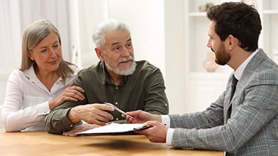 A man and his wife sitting with a lawyer getting ready to sign a document 