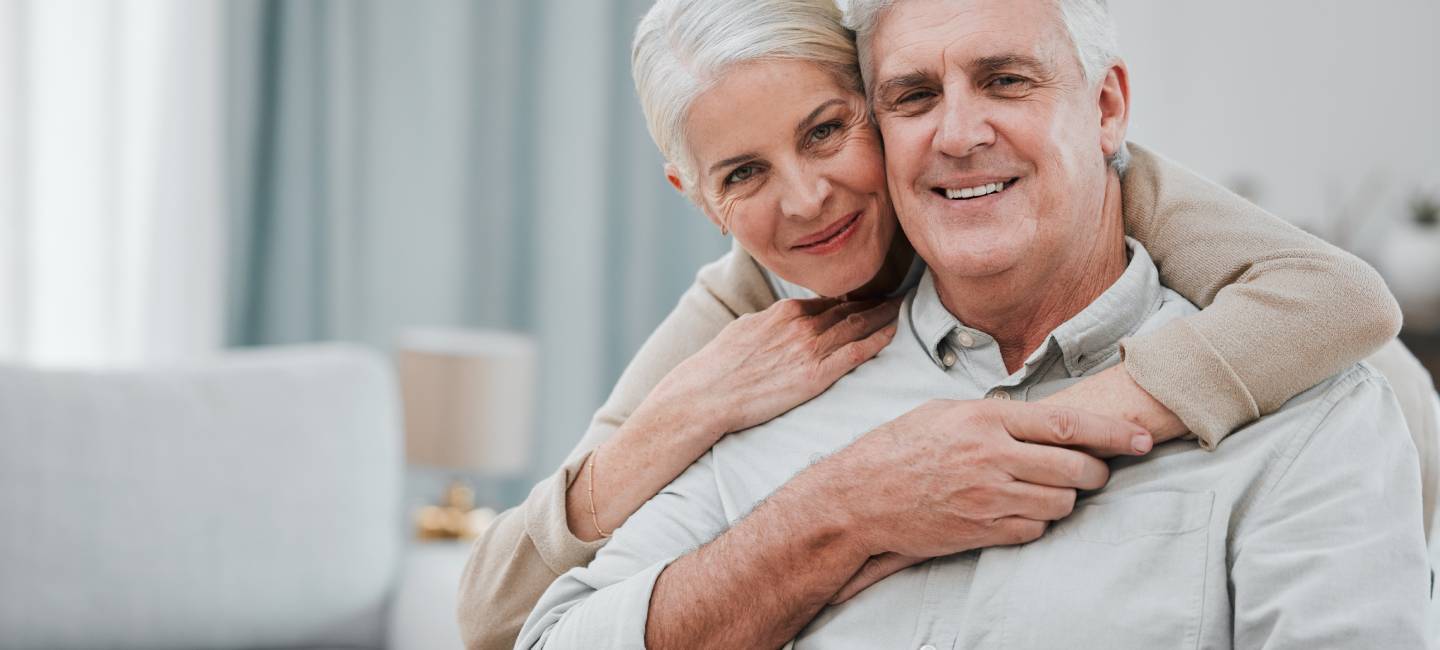 Senior couple hugging in the living room of their house together.