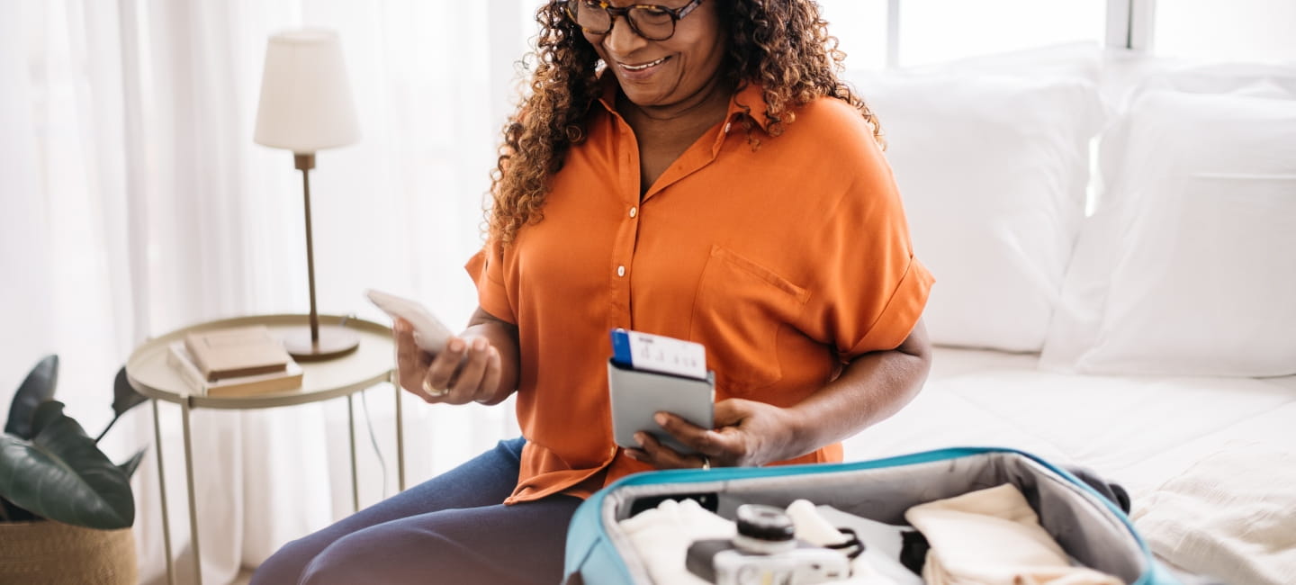 A woman holding her phone, passport and boarding pass next to an open suitcase 