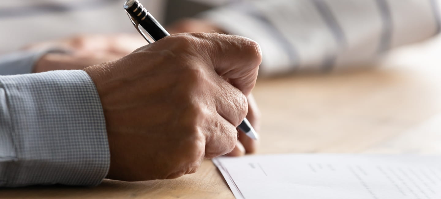 A person's hand holding a pen and writing on a piece of paper
