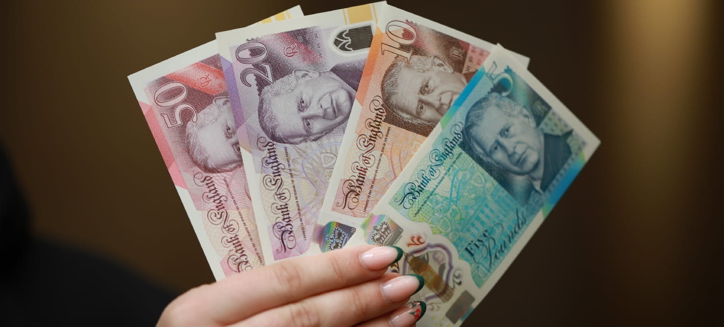 A person is holding four new bank notes with King Charles' face on it - a £50, £20, £10 and a £5 note