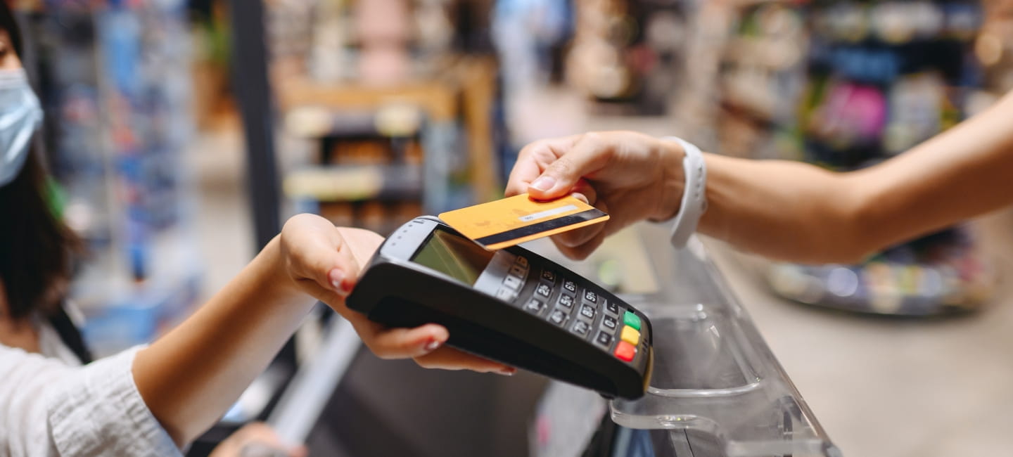 A shopkeeper is holding out a card reader and another person is tapping their card on the card reader 