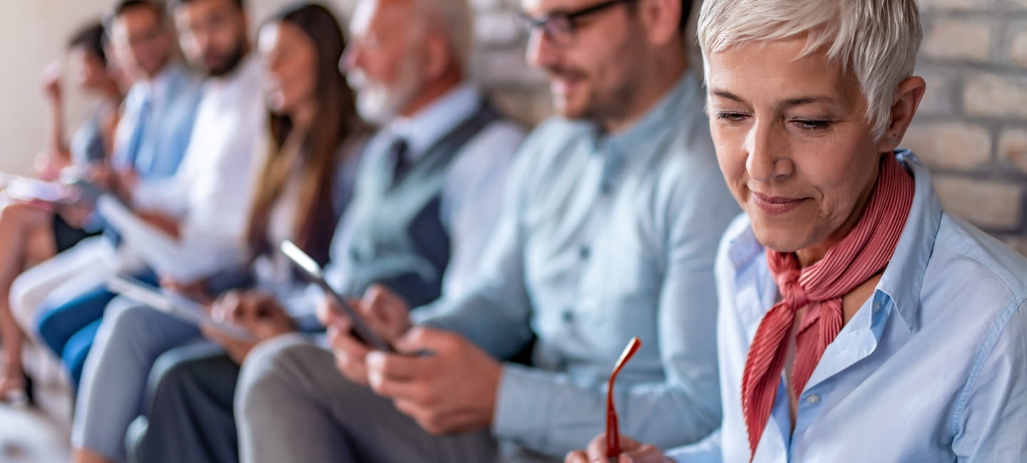 Line of people different ages sitting by wall while waiting their turn for job interview.