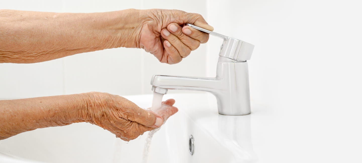 Elderly woman washes hand in bathroom