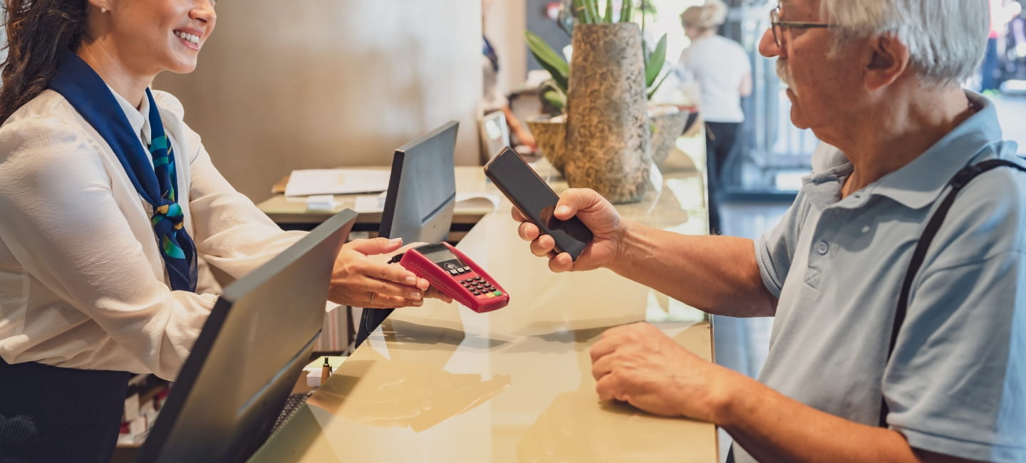 A mature couple at the hotel front desk makes contactless payments with a smartphone.