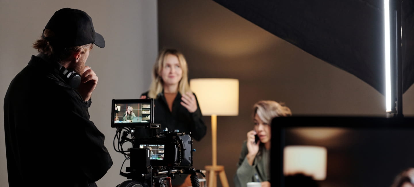 Back view of young videographer standing in front of steadicam during shooting of commercial with female model in studio