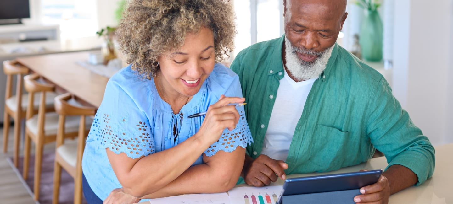 Smiling Mature Couple At Home With Digital Tablet Looking At Domestic Finances