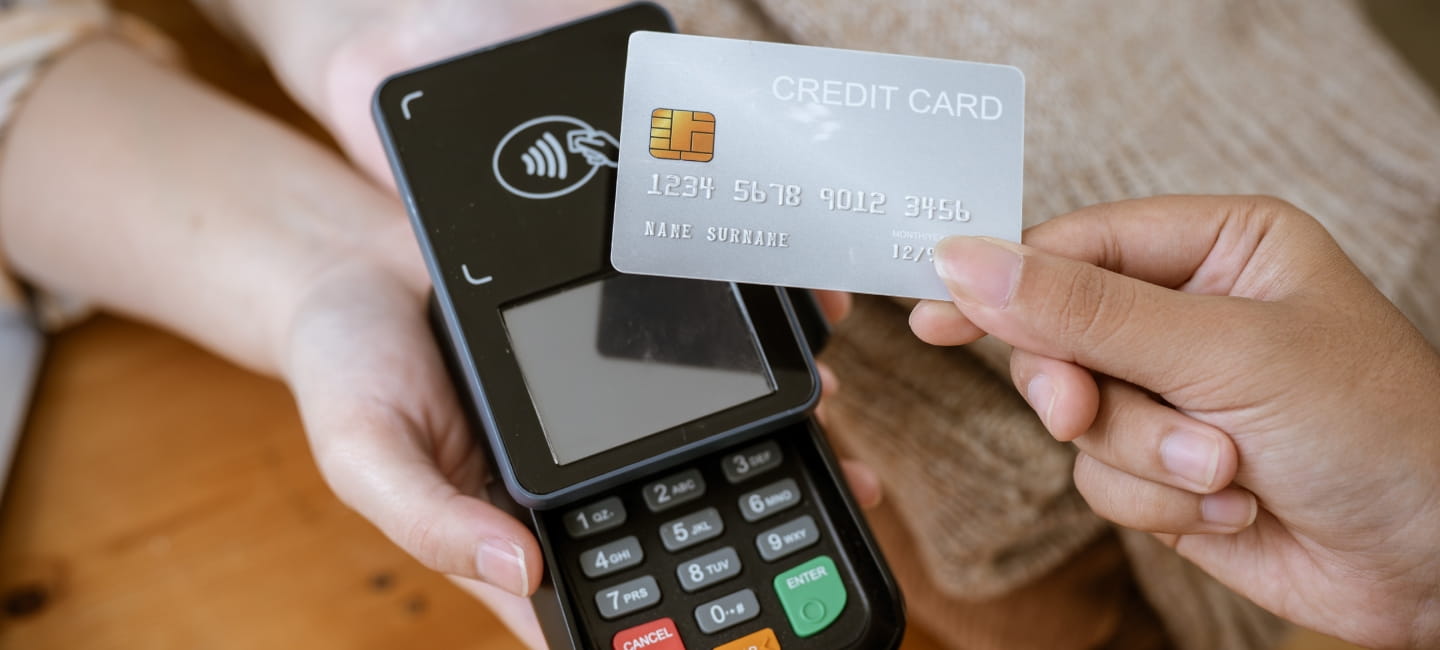 A close-up image of a customer tapping her credit card with a payment terminal or credit card machine at a cashier in a clothing store. cashless payment, card reader, electronic funds transfer