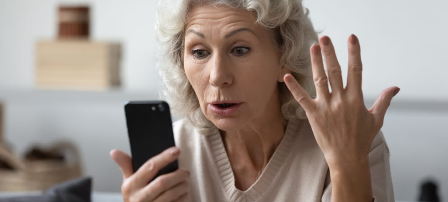 Angry shocked mature phone user staring at screen in surprise. Elderly lady worried about app error, data stealing, scam, bad news, problems with smartphone. Annoyed woman using cell for video call.