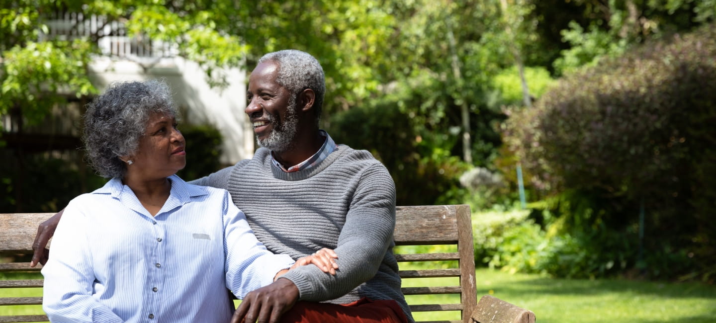 Front view of senior African American couple in the garden, sitting on a bench, embracing and talking. Family enjoying time at home, lifestyle concept.