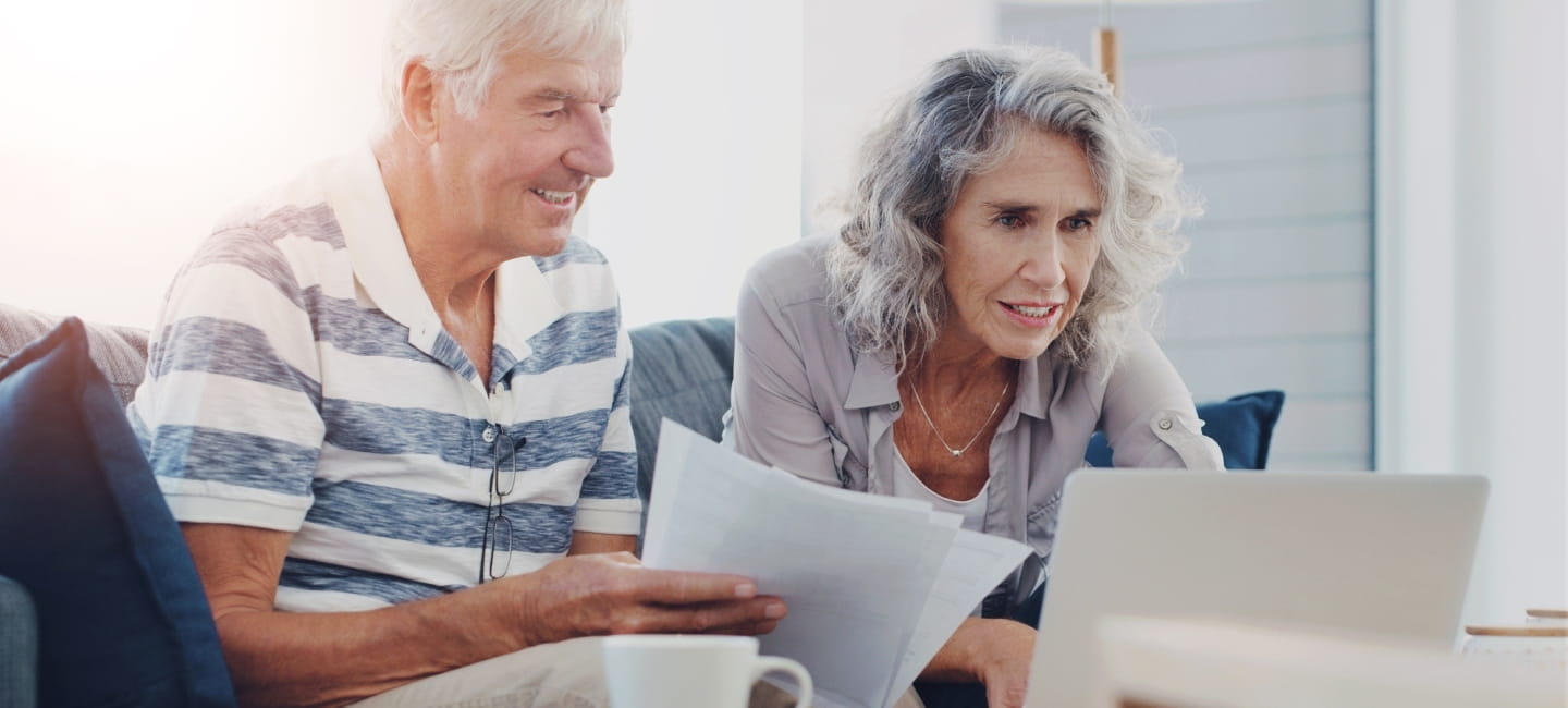 Mature couple reviewing their retirement paper work and researching on a laptop