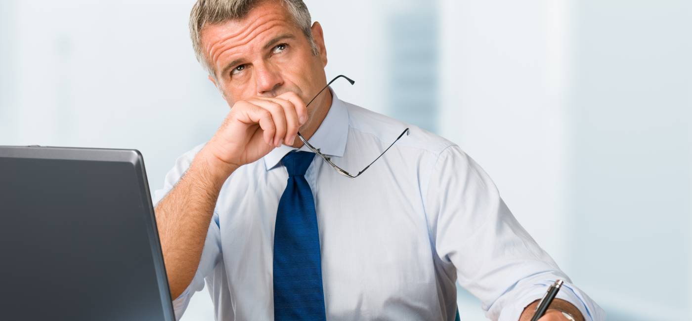 Pensive mature businessman looking up with concentration and writing in his paperwork at office