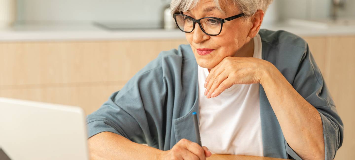 Middle aged senior woman sit with laptop and paper document, writing down pension payments