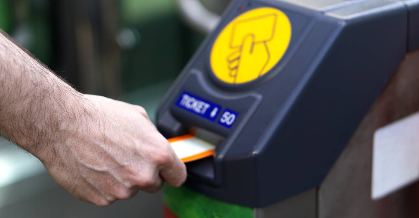 Man's hand inserting rail ticket into barrier machine