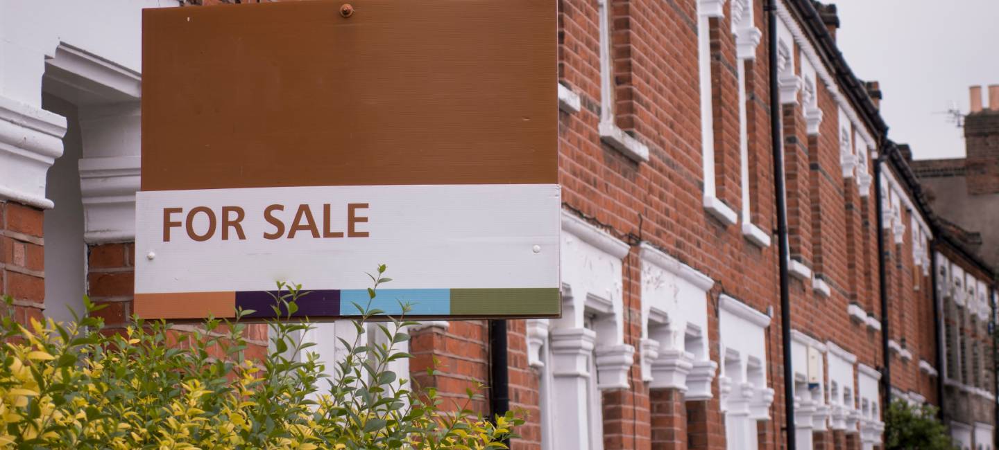 A row of red brick terraced houses with a 'for sale' sign in London
