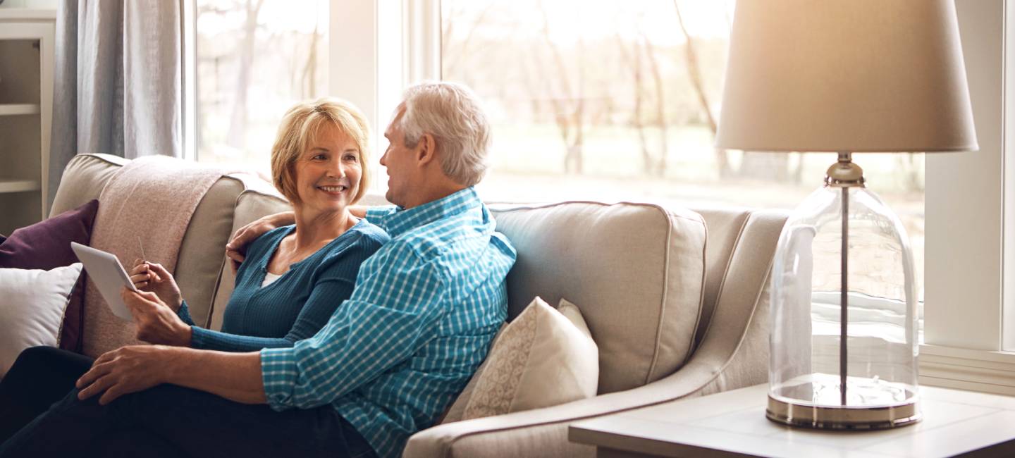 Senior couple, tablet and happy on sofa in conversation, decision and search on web in home living room. Old man, elderly woman and smile for choice with video, streaming and movie on couch in house