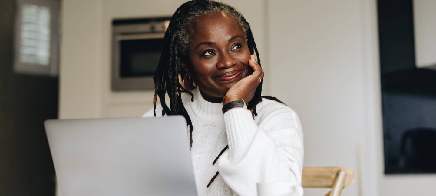 Cheerful senior businesswoman looking away thoughtfully while working on a laptop at home