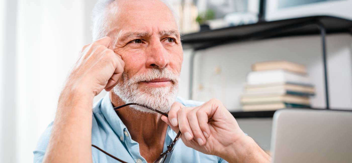 ired mature 60s man working at laptop from home, taking off glasses, touching head and eyes.