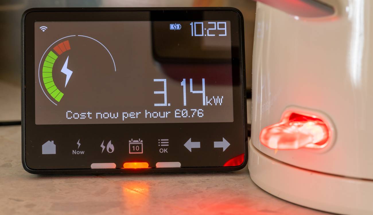A energy use and cost concept with a smart energy meter showing the amount of energy in use next of a kettle boiling water.