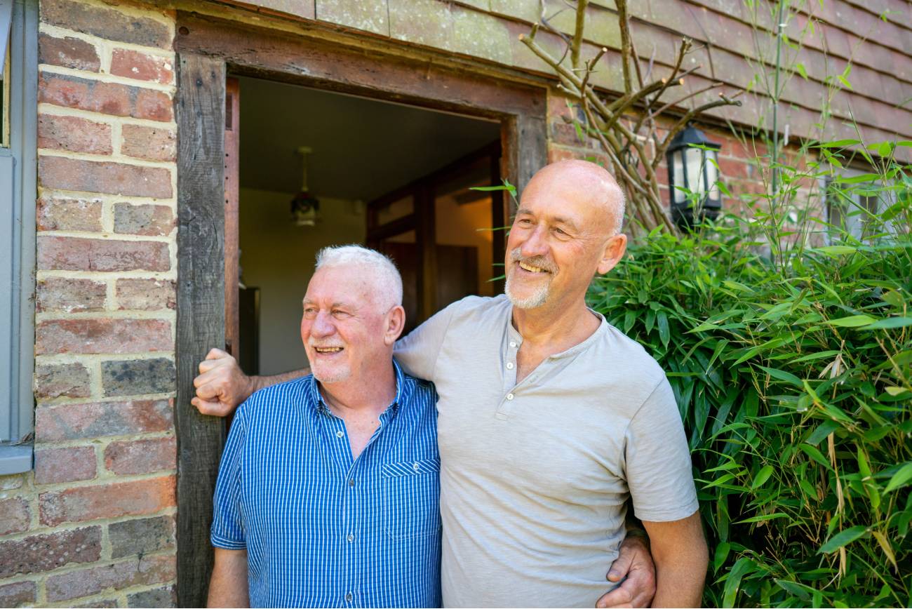 Smiling senior male couple standing in front of house