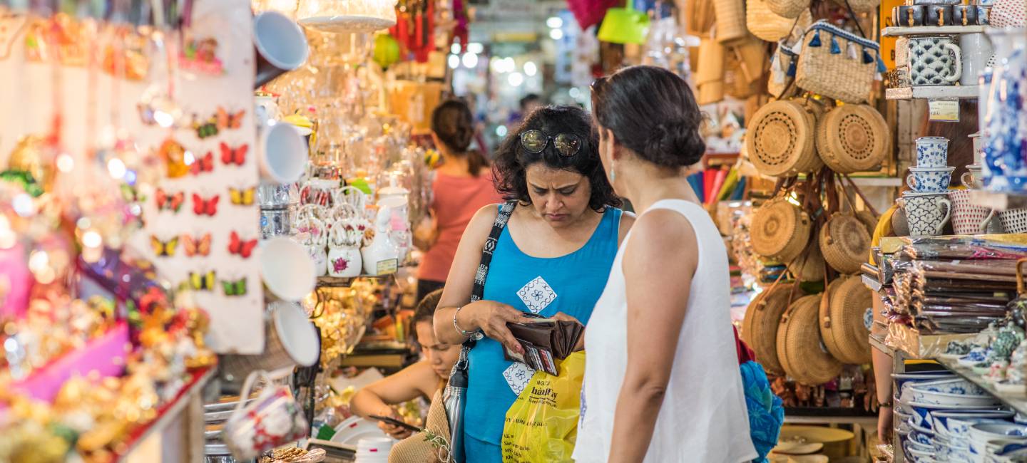2 woman travelers buy souvenirs in a shop in Ben Thanh Market, one of them checks money in her wallet. Ben Thanh Market is a famous Saigon touristy shopping area