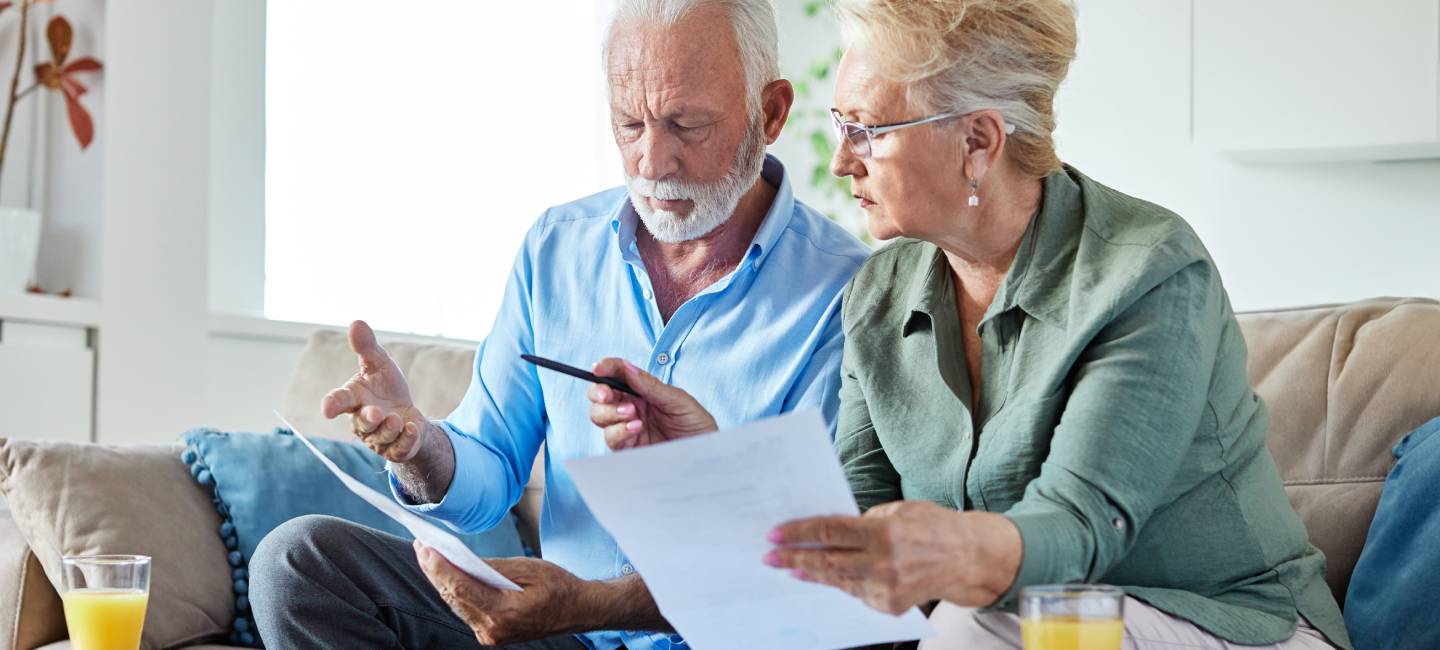 Senior couple checking bills and calculating expenses using a calculator at home, debt taxes and home budget concept, worried married elderly couple