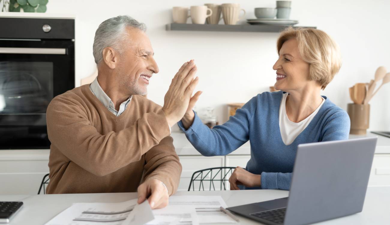 Happy married couple high five each other after paying utility bills or mortgage loan. Concept of profitable investment, social benefits, pension contributions and deposits