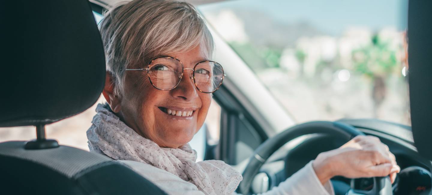 Happy owner. Handsome mature woman sitting relaxed in his newly bought car looking at the camera smiling joyfully. One old senior driving and having fun.