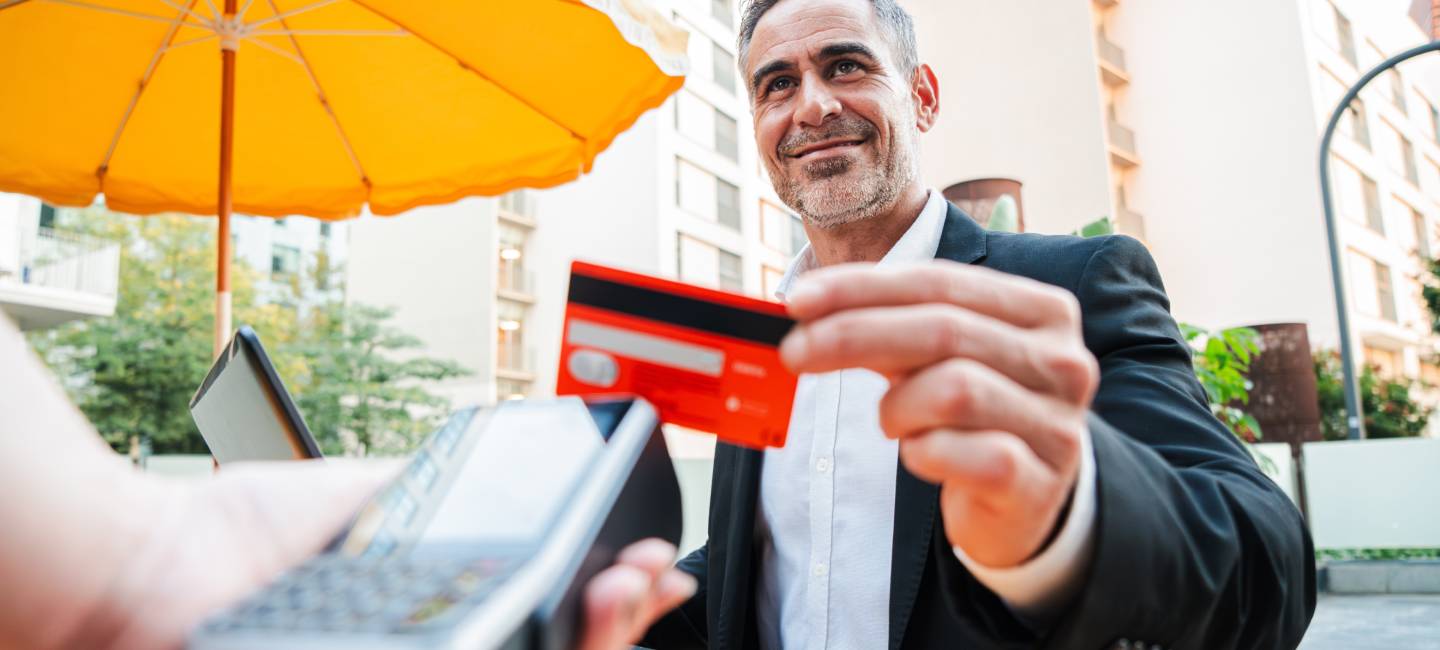 Happy mature business man paying bill using a contactless credit card in a restaurant.