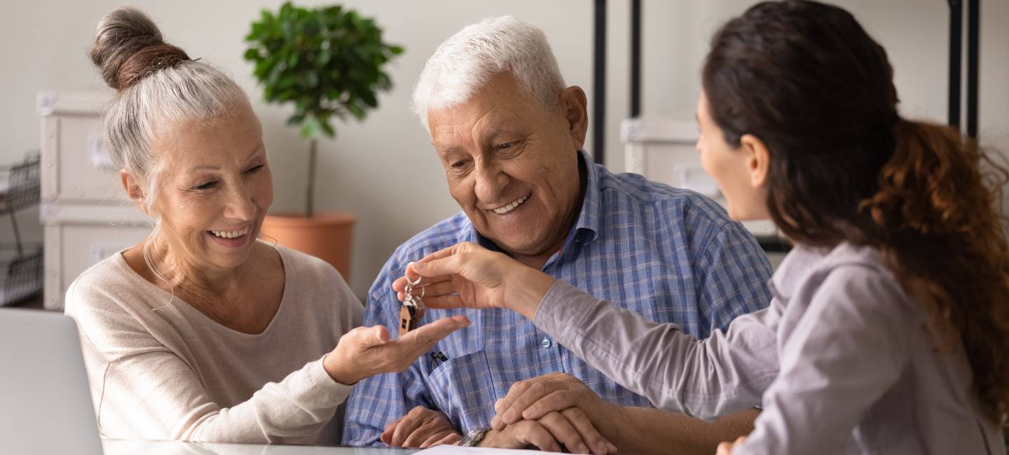 Retired couple buy house. Excited senior husband wife become homeowners receive keys from new home in realtor office. Overjoyed happy mature spouses realty buyers get key from agent after closing deal