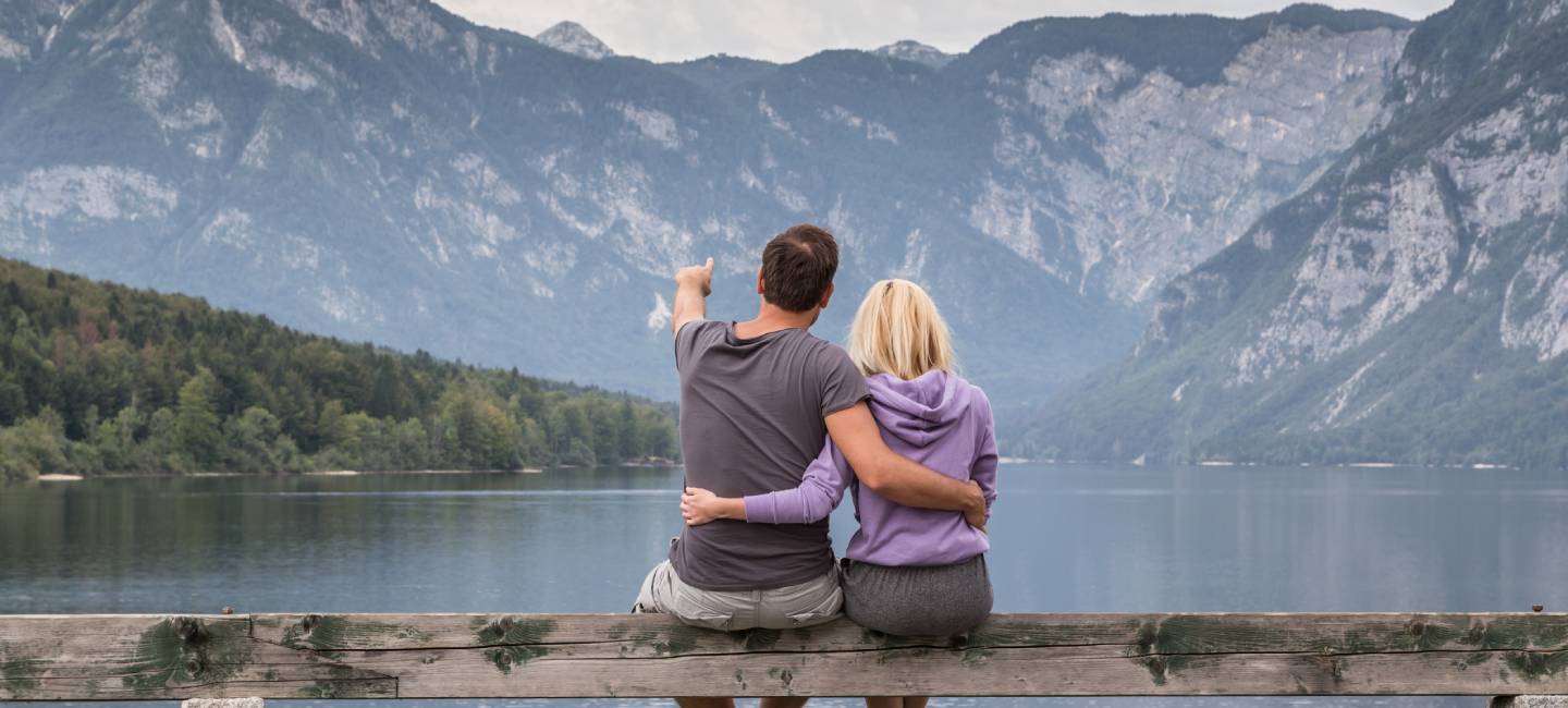 Embraced casual couple watching tranquil overcast morning scene at lake Bohinj, Alps mountains, Slovenia.