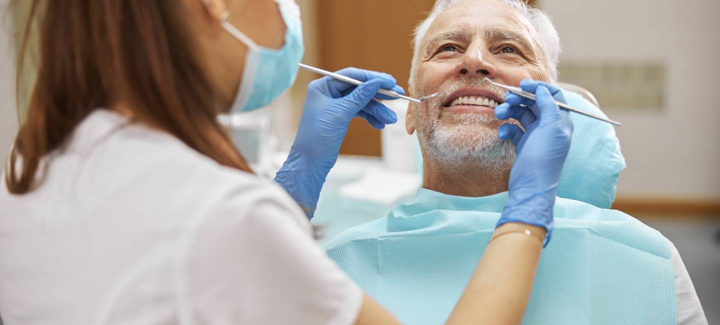 Skillful young female dentist holding dental tools while examining an elderly man