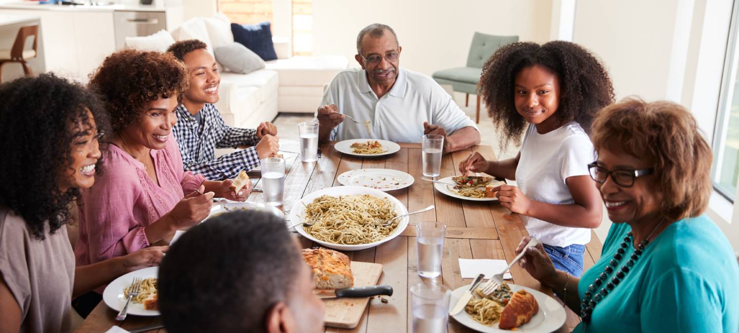 Three generation black family sitting at the table talking and eating dinner together, close up