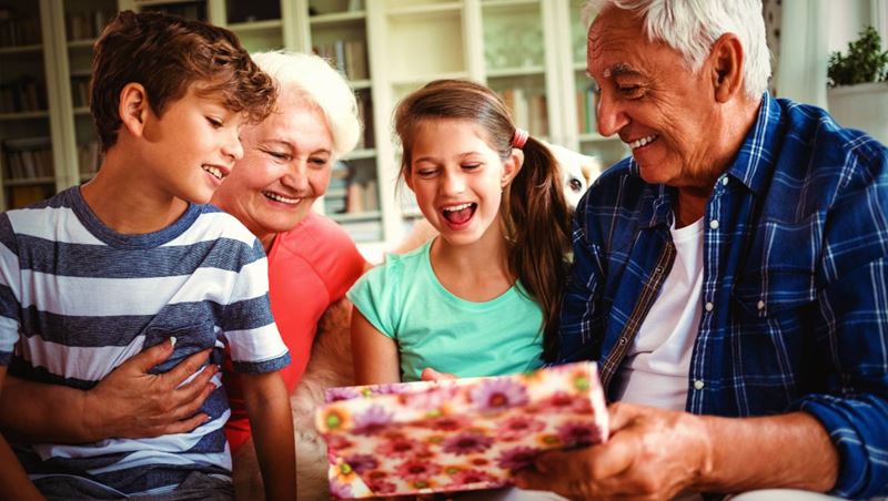 Grandparents and grandchildren looking at surprise gift in living room at home