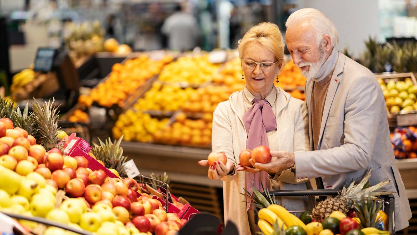 Cheerful senior couple is choosing apples at the supermarket.
