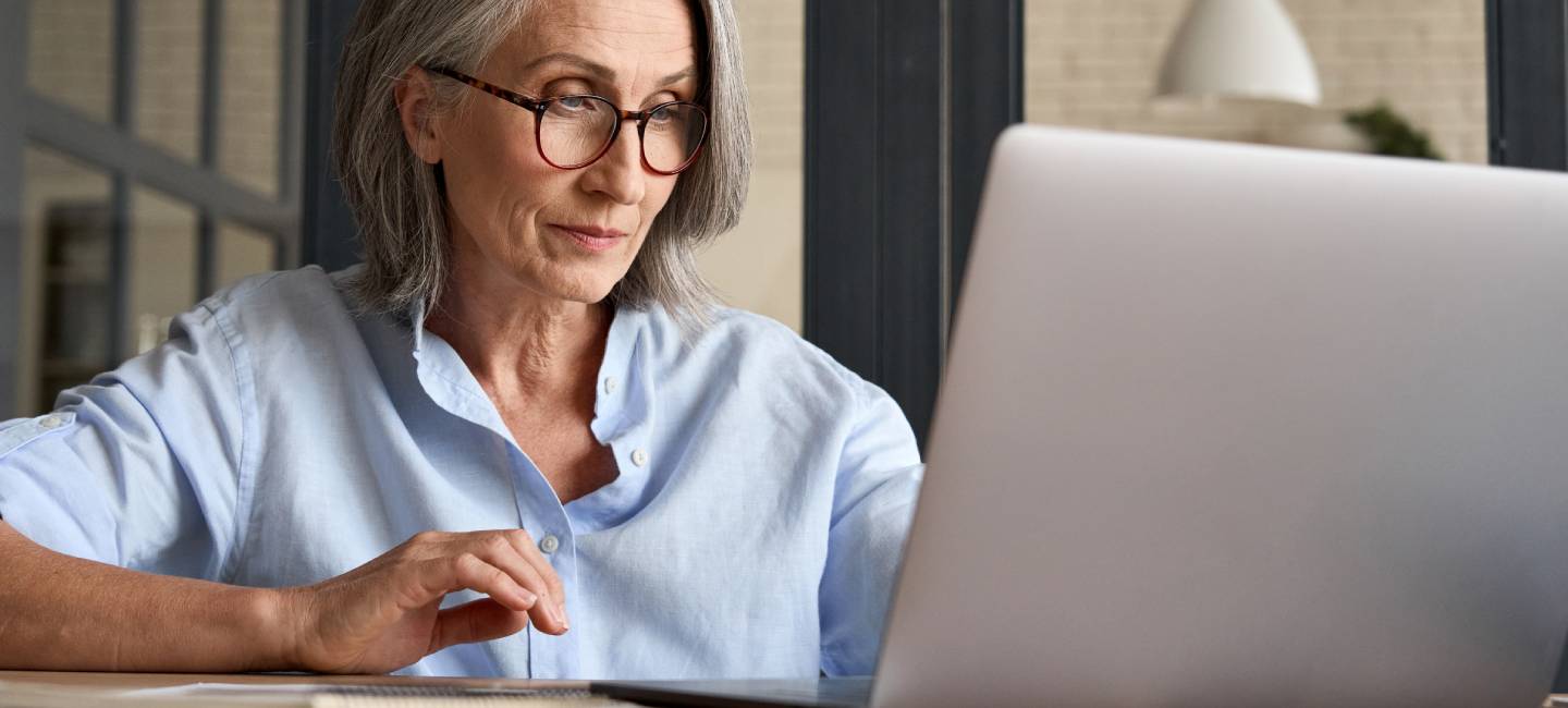 Mature woman in her 60s looking at information on her laptop and looking thoughtful.
