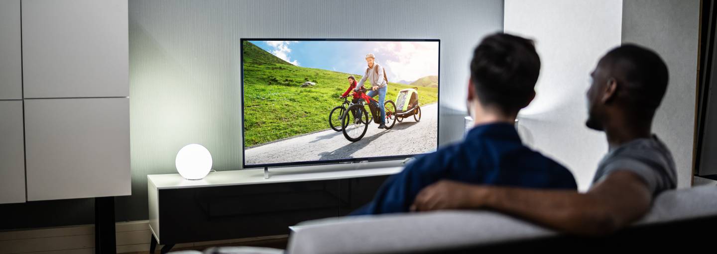 Two men watching cycling on television, sitting on the sofa together