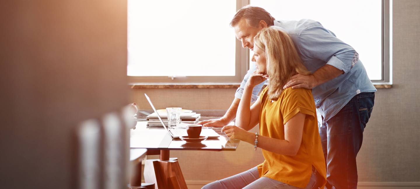 A mature couple sitting at their dining room table doing online banking using a laptop.