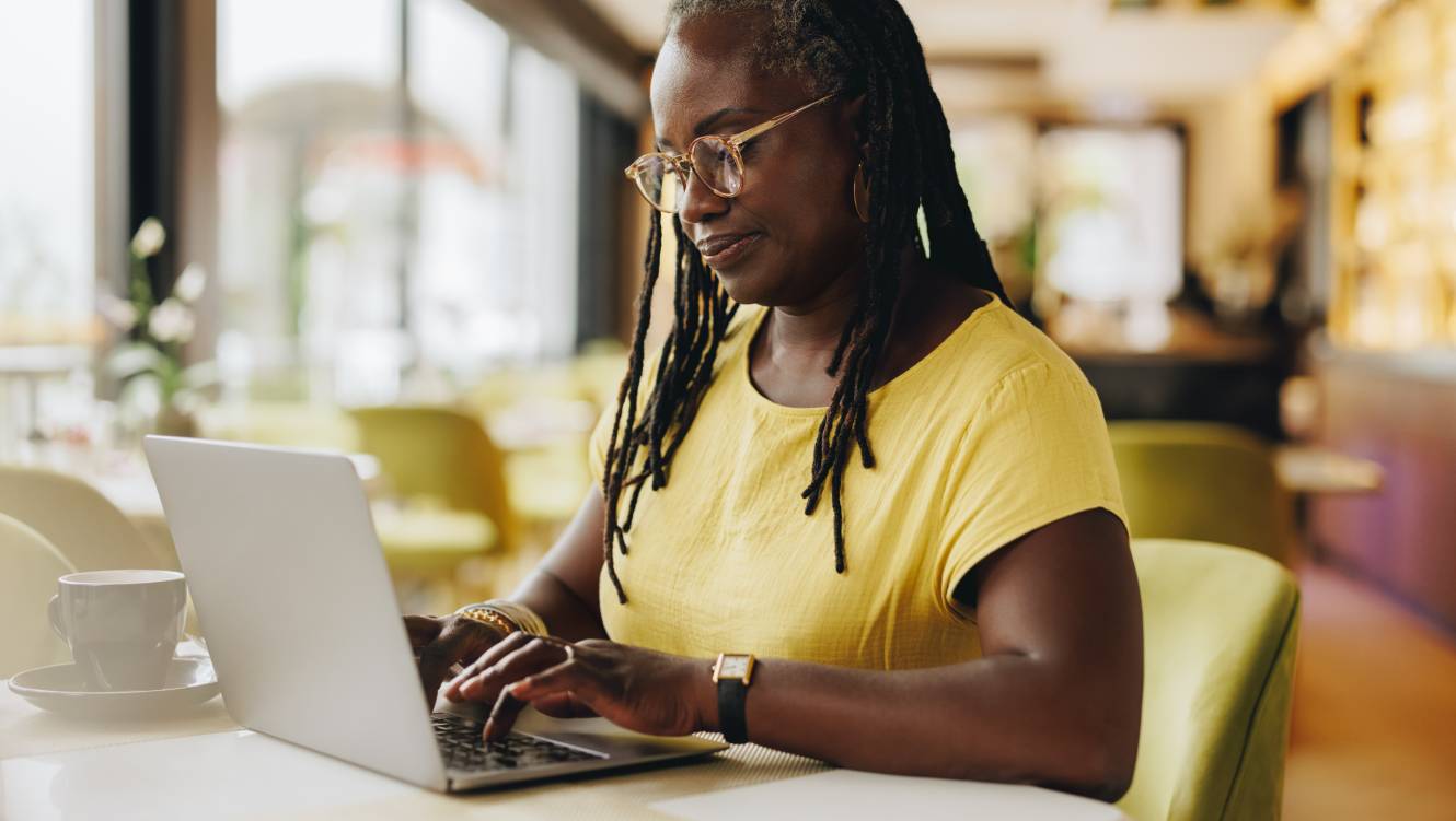 Woman in a yellow top and glasses, sitting at a table on the laptop 
