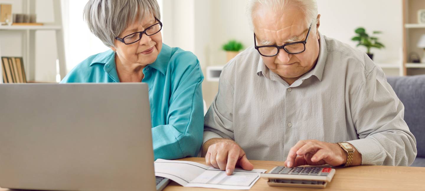 Mature couple sitting at home at the desk with laptop and bills calculating finances or taxes