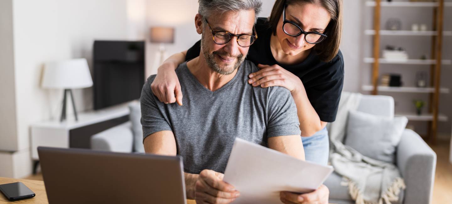 Mature couple looking at paper work with a laptop to the side, looking over taxes and budgets